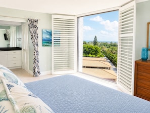 Une chambre avec une grande fenêtre, un lit, une commode et une salle de bain avec douche.