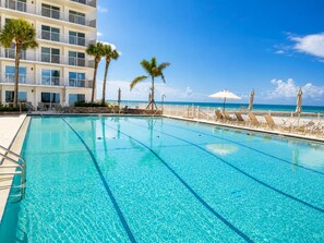 A clear blue swimming pool with lounge chairs and umbrellas, a white building with balconies, and a view of the ocean. - 2 bedroom 2 bath Luxury Beachfront condo on Longboat Key (Longboat Key)
