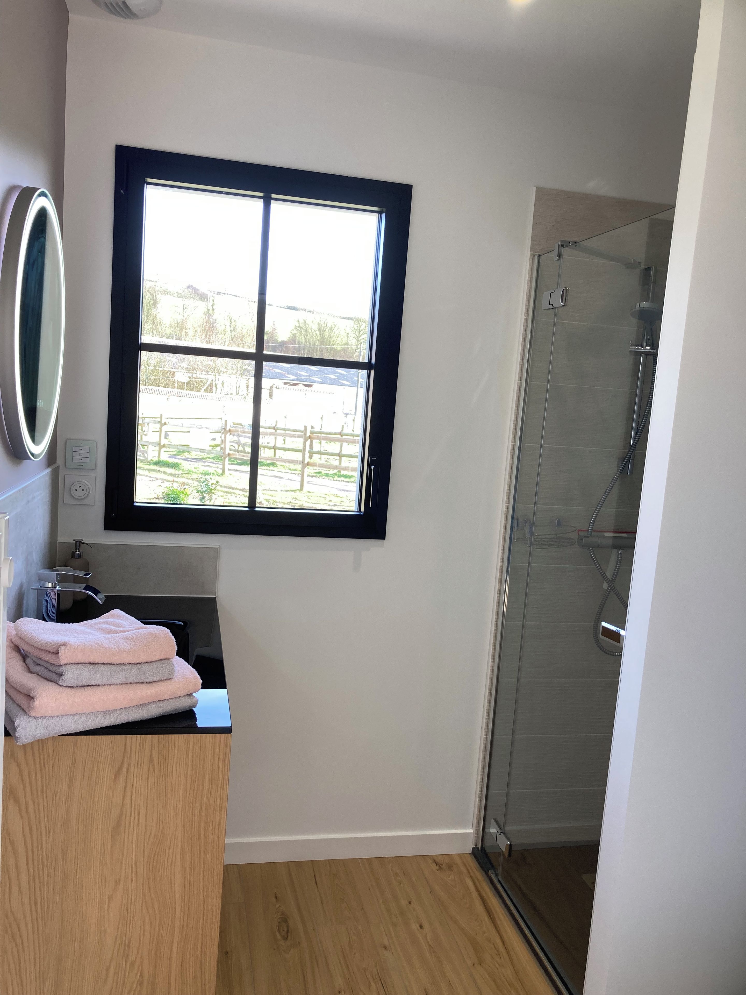 Ein Badezimmer mit Fenster, Spiegel, Waschbecken und Dusche.