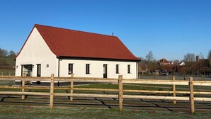 Ein eingeschossiges Gebäude mit rotem Dach und weißen Wänden, umgeben von einem Holzzaun.
