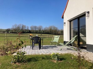 A patio with a table and chairs, a small garden, and a view of a fenced field with trees.