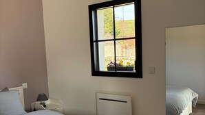 Ein Schlafzimmer mit einem Bett, einem Nachttisch, einer Lampe, einer Heizung, einem Fenster und einem Spiegel.