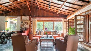 A rustic interior with a wooden ceiling, a sofa set, a dining table, and a window with a view of greenery. - Cabanas VillaRejo (Jarinu)