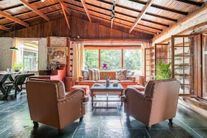 Un interior rústico con techo de madera, un conjunto de sofás, una mesa de comedor y una ventana con vistas a la vegetación.
