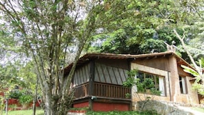 A rustic wooden house with a balcony, surrounded by lush greenery. - Cabanas VillaRejo (Jarinu)