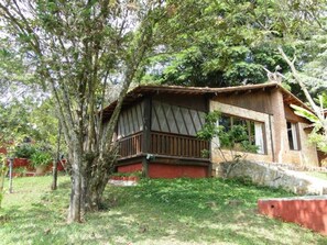 Una casa de madera rústica con balcón, rodeada de abundante follaje.