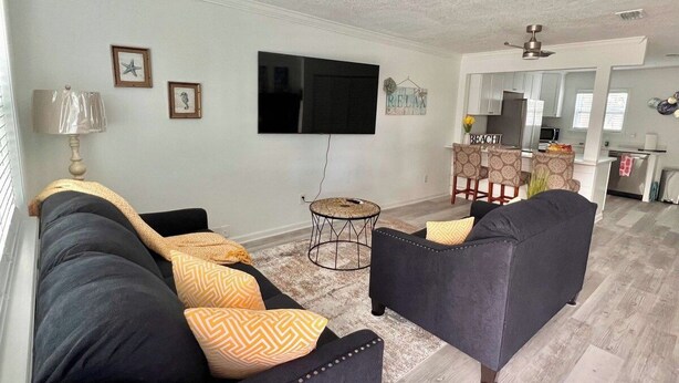 A living room with a sofa set, a television, and a small round table. - Be A Nomad | Cozy 2br Home Steps from the Beach (Jacksonville Beach)