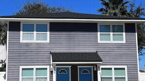 A two-story house with a dark gray exterior, a blue front door, and a small porch area. - Be A Nomad | Cozy 2br Home Steps from the Beach (Jacksonville Beach)