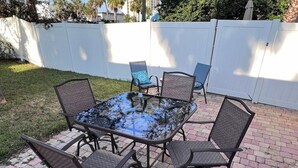 An outdoor patio with a glass-top table surrounded by six chairs. - Be A Nomad | Cozy 2br Home Steps from the Beach (Jacksonville Beach)
