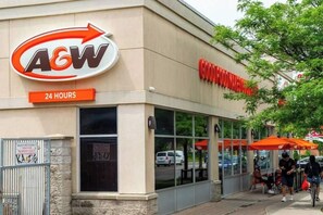 En butiksvindue med et stort A&W logo, et skilt der viser døgnåbent og en tydelig indgang.