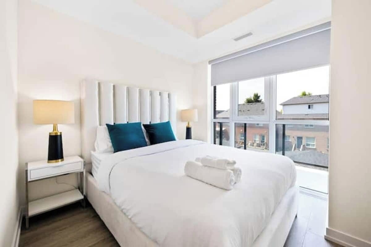 A hotel room with a large bed, two bedside tables, a window with a view, and a modern headboard.
