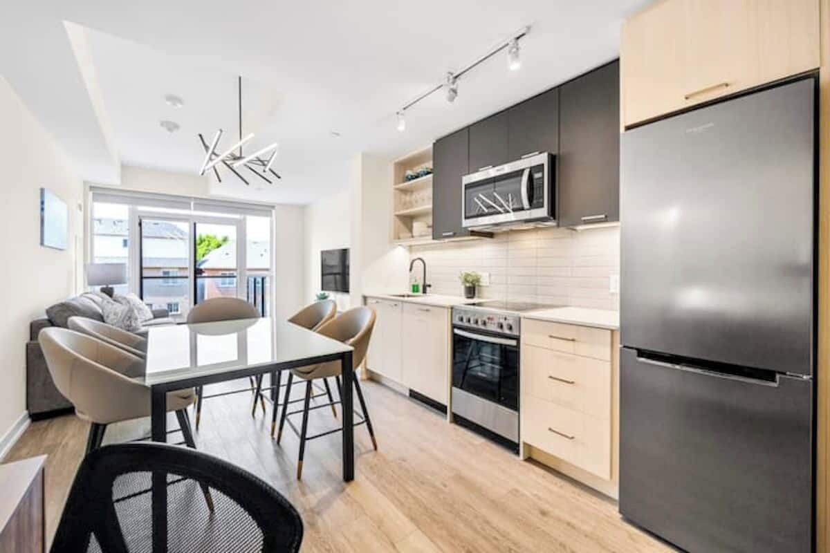 A modern kitchen with a dining area, stainless steel appliances, and a large window.