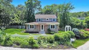 A two-story house with a front porch, a small garden, and a white picket fence. - Charming Mattituck Retreat Near the Bay with Modern Updates (Mattituck)