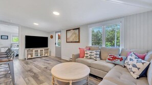 A living room with a sofa, television, and a round table. - Charming Mattituck Retreat Near the Bay with Modern Updates (Mattituck)