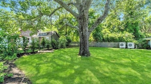 A backyard with a large tree, a lawn, a house, and a fence. - Charming Mattituck Retreat Near the Bay with Modern Updates (Mattituck)