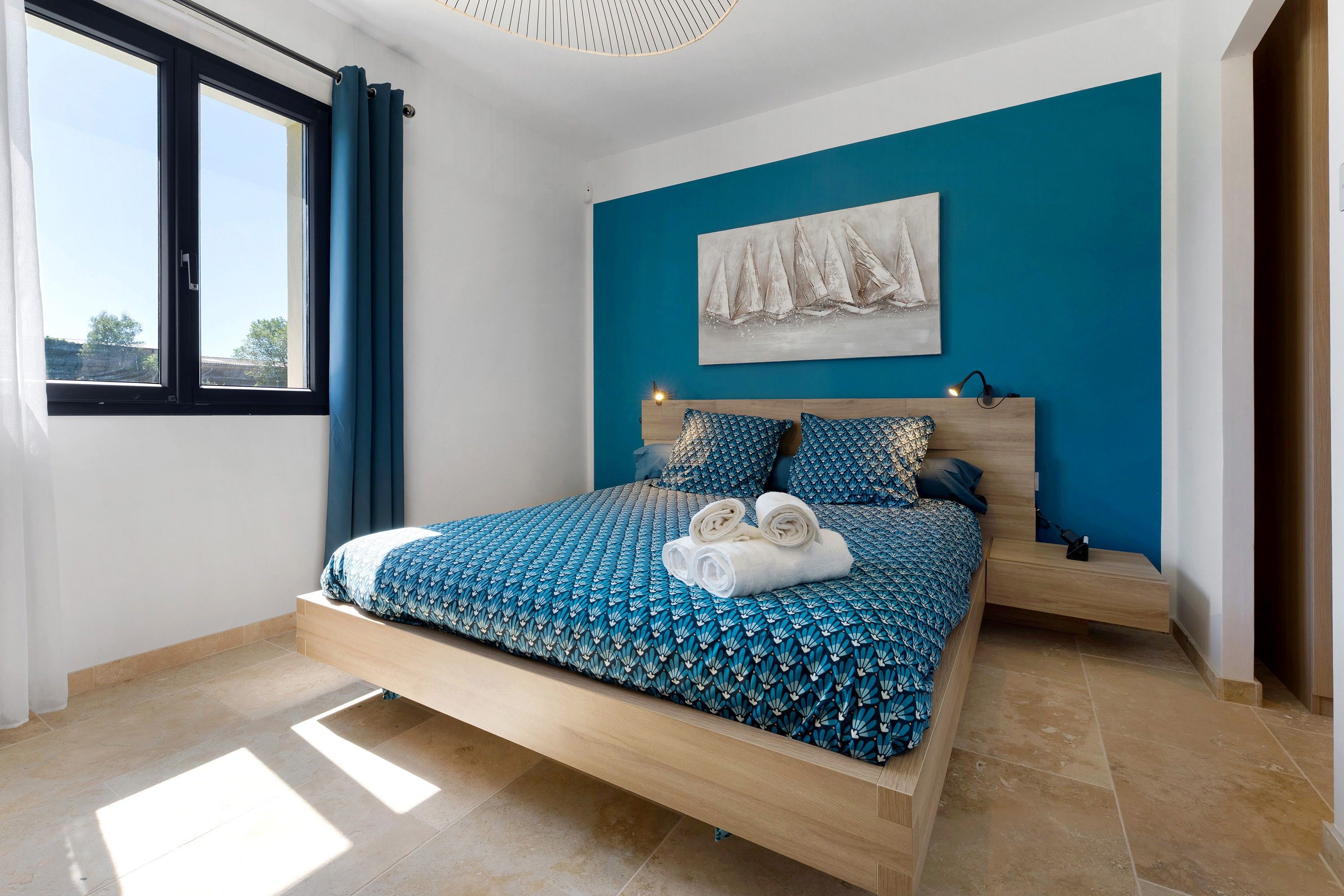 Une chambre à coucher moderne, avec un lit, une table de chevet, une lampe fixée au mur et une fenêtre avec des rideaux.