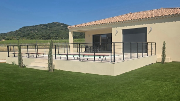 Un edificio moderno con tetto piatto, un patio coperto con panche e vista su un paesaggio collinare.
