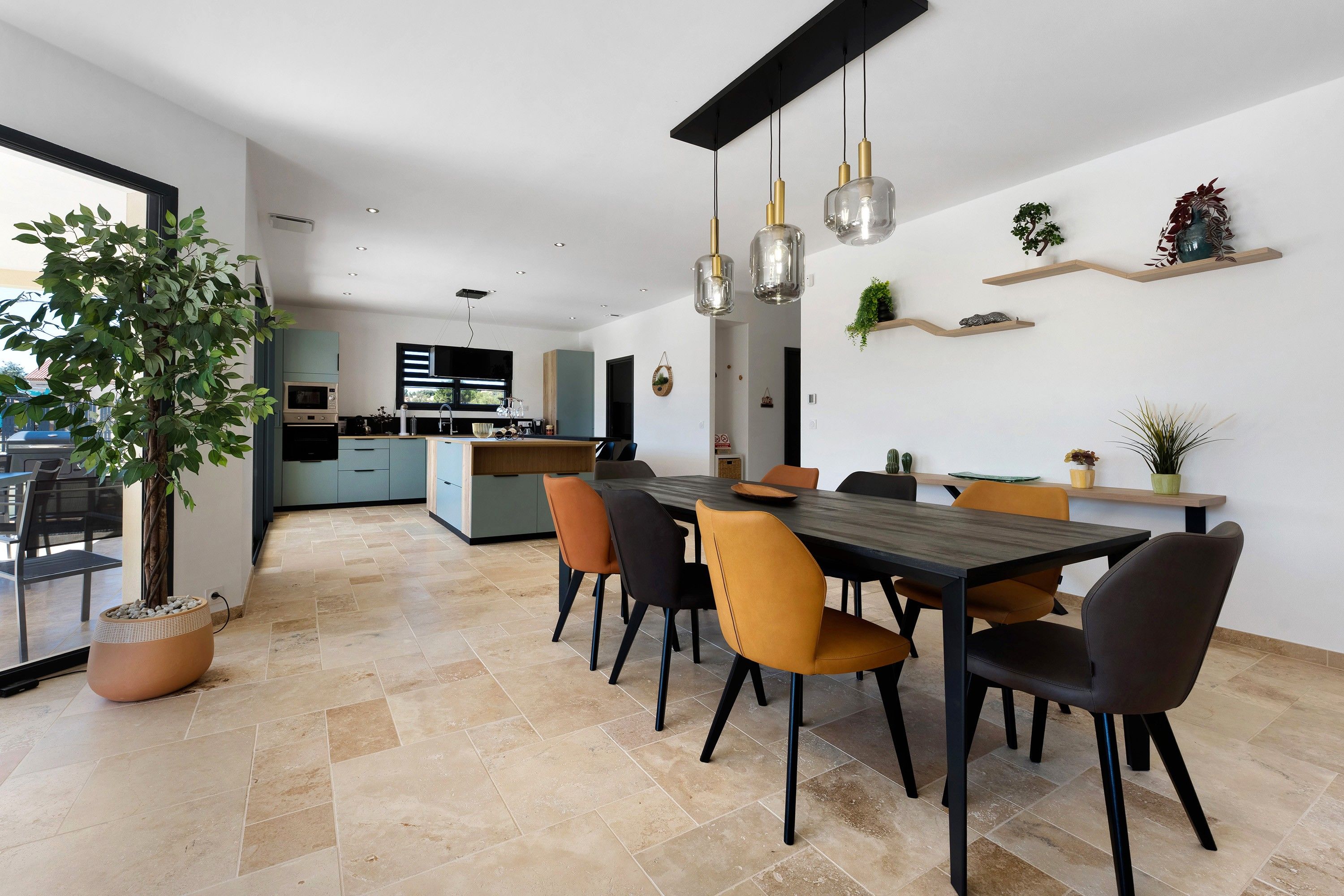 Une cuisine moderne avec un coin repas, comprenant un grand îlot central, des luminaires suspendus et des plantes en pot.