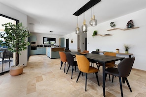 Cocina moderna con comedor, que incluye una isla grande, iluminación colgante y plantas en macetas.