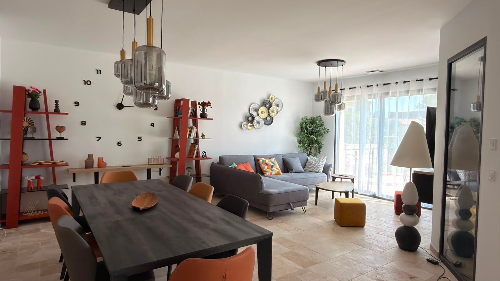 Una sala moderna con comedor, un sofá gris y una estantería roja.