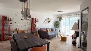A modern living room with a dining area, a grey sofa, and a red bookshelf.