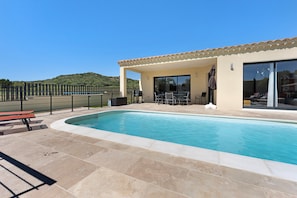A swimming pool with a patio area, outdoor seating, and a view of a hilly landscape.