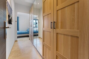 A hallway leading to a bedroom with a bed, wooden wardrobe, and a bathroom with a shower.