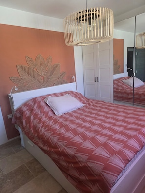 Une chambre à coucher avec un lit, un miroir et un luminaire fixé au mur.