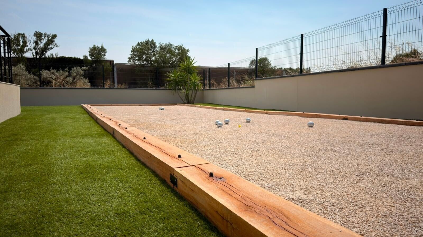 Un campo de croquet con borde de madera, superficie de grava y una cerca de alambre en el fondo.