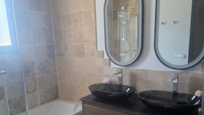 Un bagno con una vasca, due specchi, un lavandino nero e piastrelle decorate.