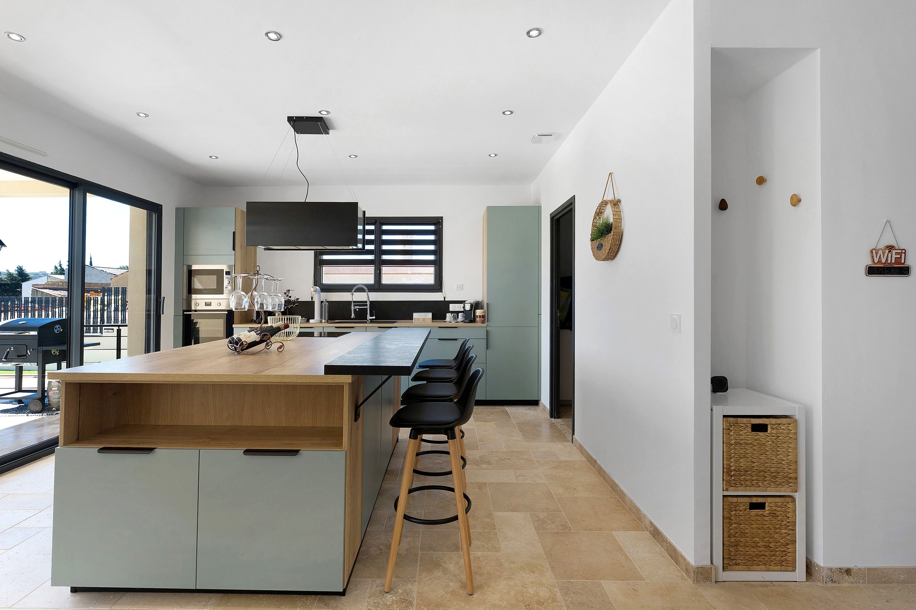 A modern kitchen with a central island, bar stools, and a large window.