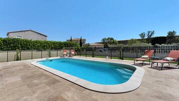 Une piscine rectangulaire avec une terrasse carrelée, entourée d’une petite clôture et d’une haie.