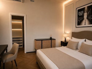 A hotel room with a bed, a desk, a chair, a nightstand, and a framed picture on the wall. - Five Suites 1 (Milan)
