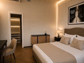 Habitación de hotel con cama, escritorio, silla, mesita de noche, lámpara y un cuadro en la pared.