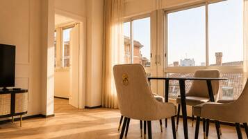 Una sala moderna con televisor, una mesa de comedor con sillas y ventanas grandes con vista a la ciudad.