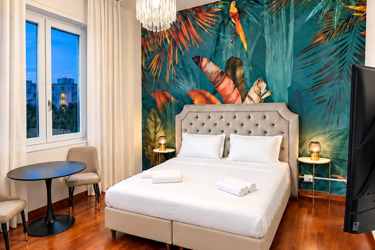 A hotel room with a large bed, a round table, a chair, a TV, and a window with curtains.