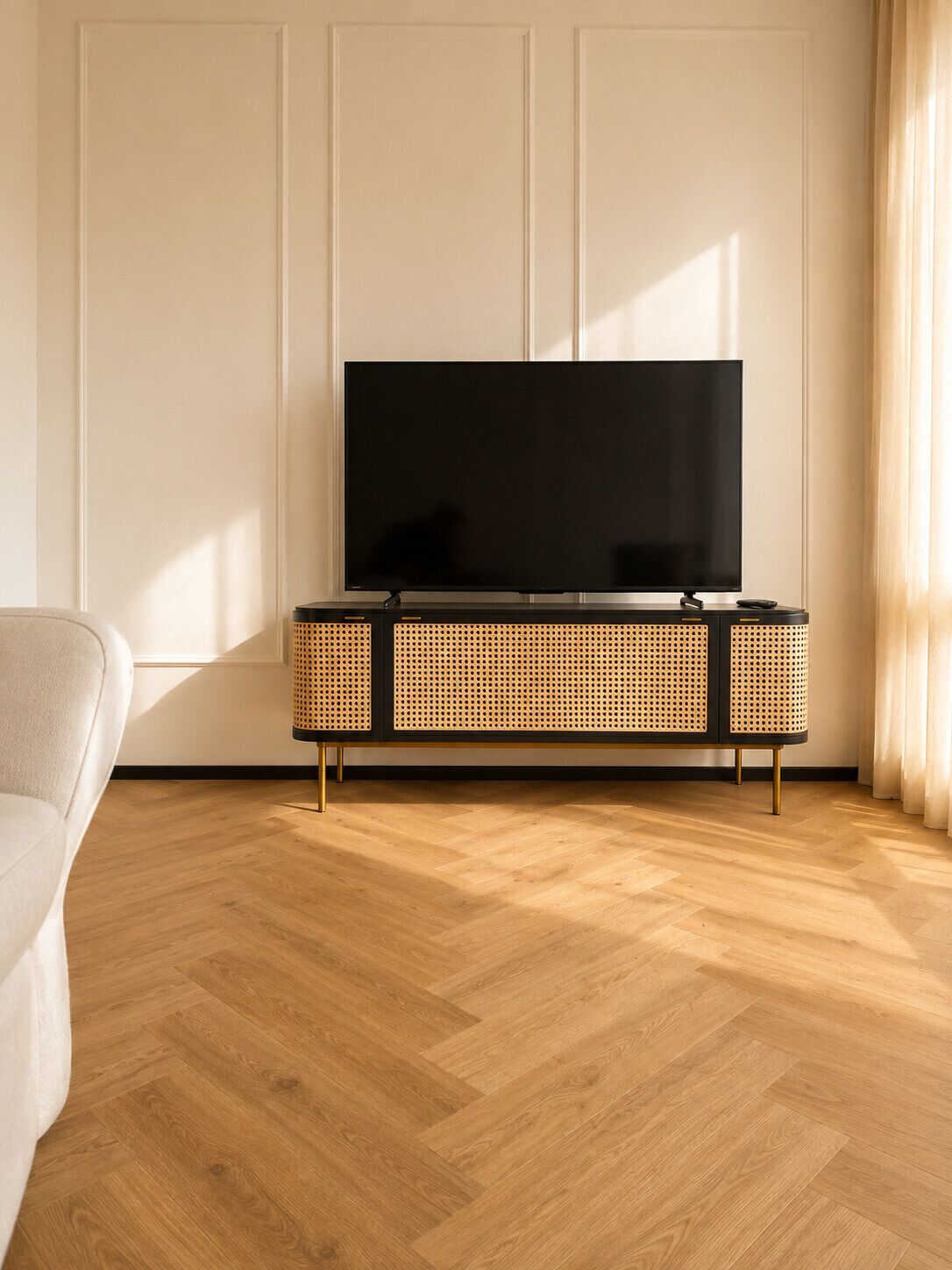 Una sala de estar moderna con un televisor de pantalla plana sobre una consola negra y de mimbre, piso de parqué de madera y una pared blanca.