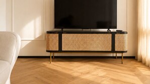 A modern living room with a flat-screen TV on a black and wicker console, wooden parquet flooring, and a white wall. - Five Suites 1 (Milan)