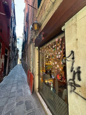 A narrow street with buildings on either side, a shop with a display of colorful items, and a closed shop with a window decorated with hanging ornaments. - Room 1 with Wi-Fi and Air Conditioning (Venezia)