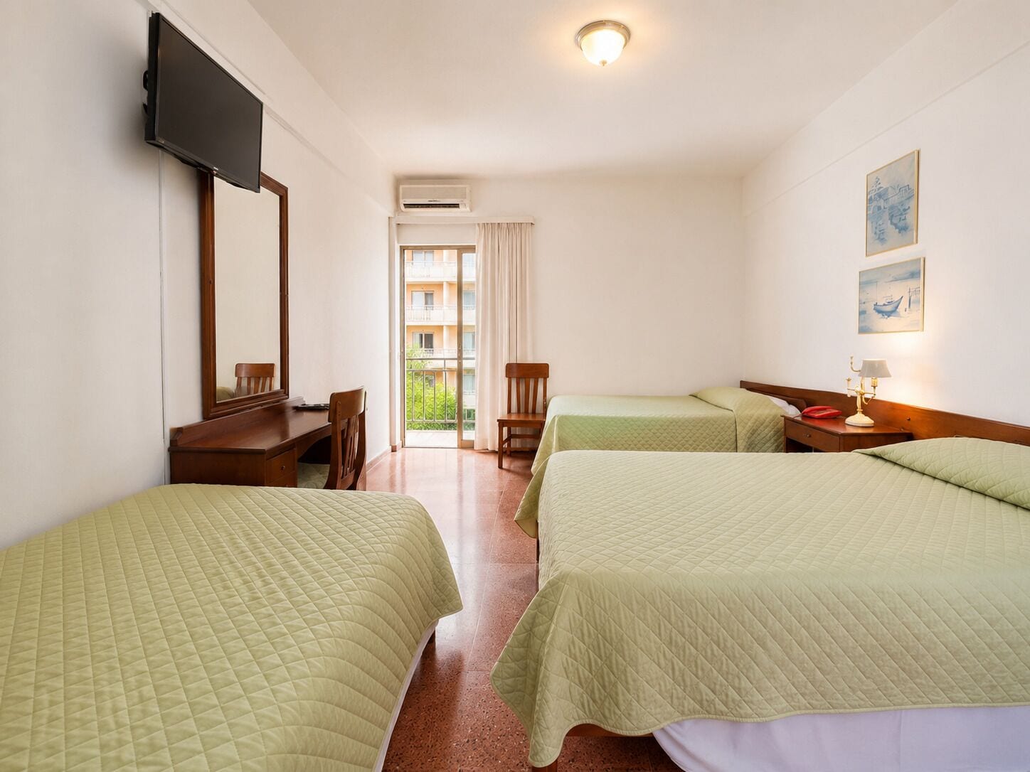 A hotel room with two beds, a desk, a chair, a television, and a window with a view of a balcony.