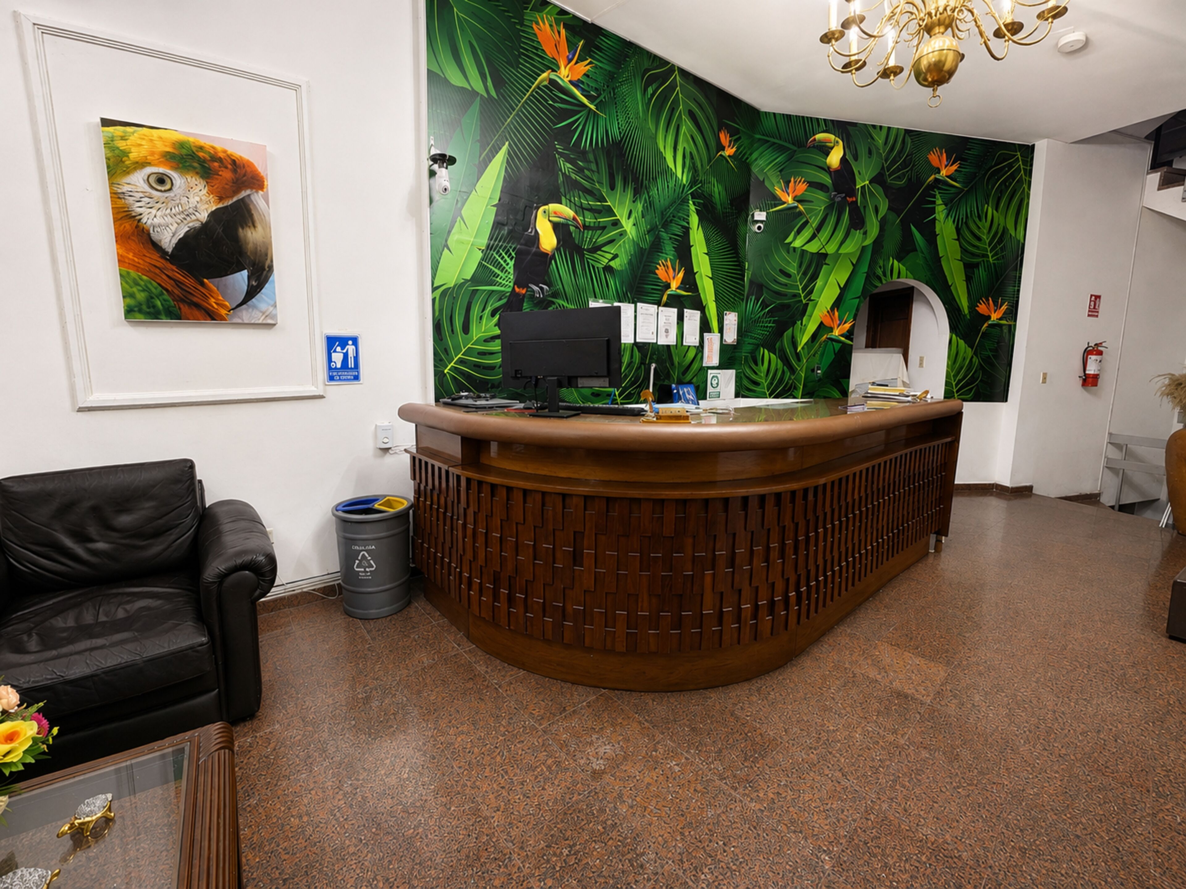 A reception desk with a wooden finish, a framed wildlife painting, and a green leaf-patterned wall mural.