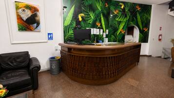 A reception desk with a wooden finish, a framed wildlife painting, and a green leaf-patterned wall mural.