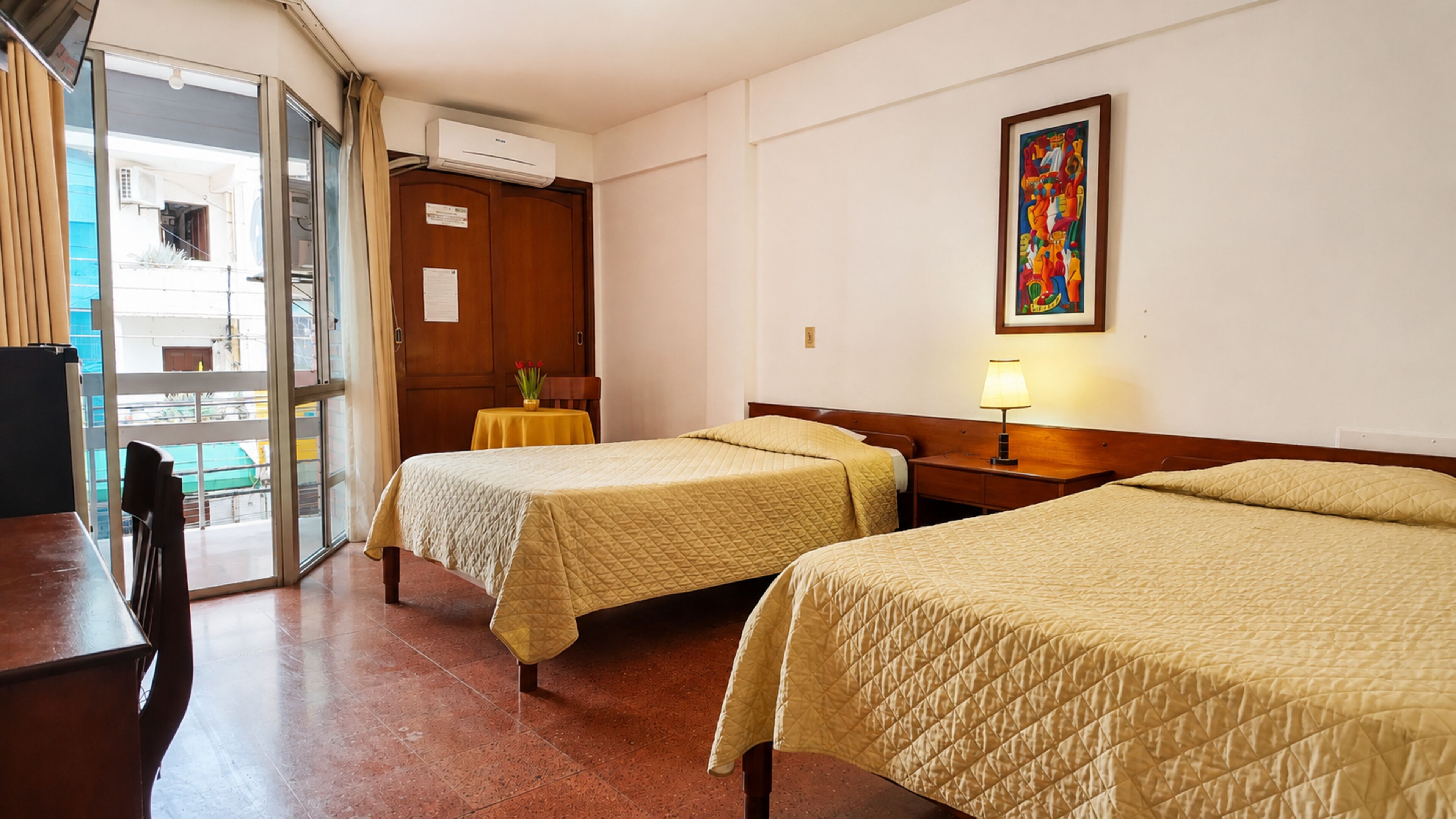Habitación de hotel con dos camas, una mesa, una silla, un equipo de aire acondicionado y un cuadro en la pared.