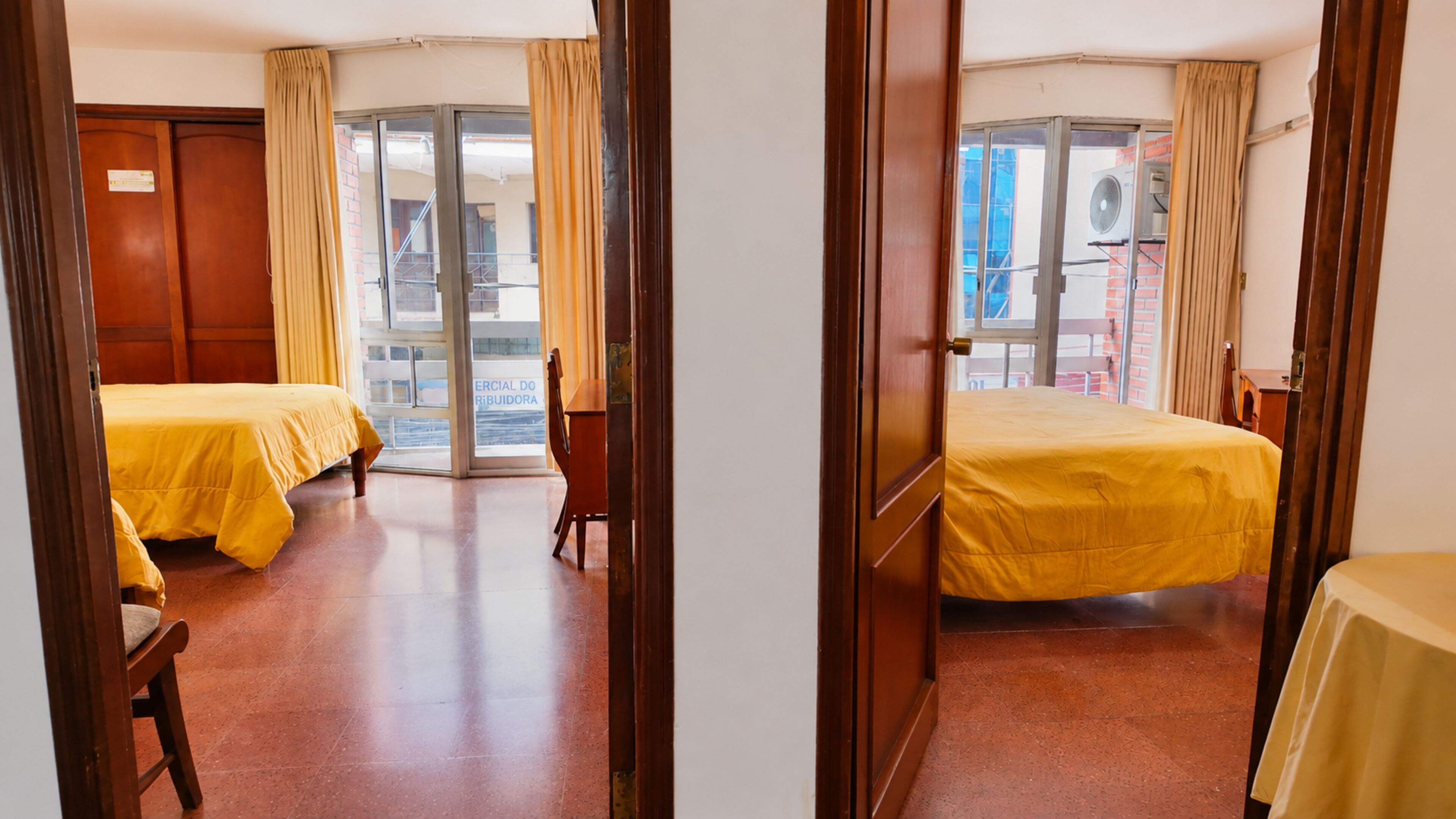 A hotel room with two beds, a wooden wardrobe, and a sliding glass door leading to an outdoor area.