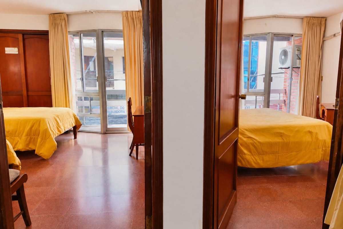 Quarto de hotel com duas camas, um guarda-roupa de madeira e uma porta de vidro deslizante que dá para uma área externa.