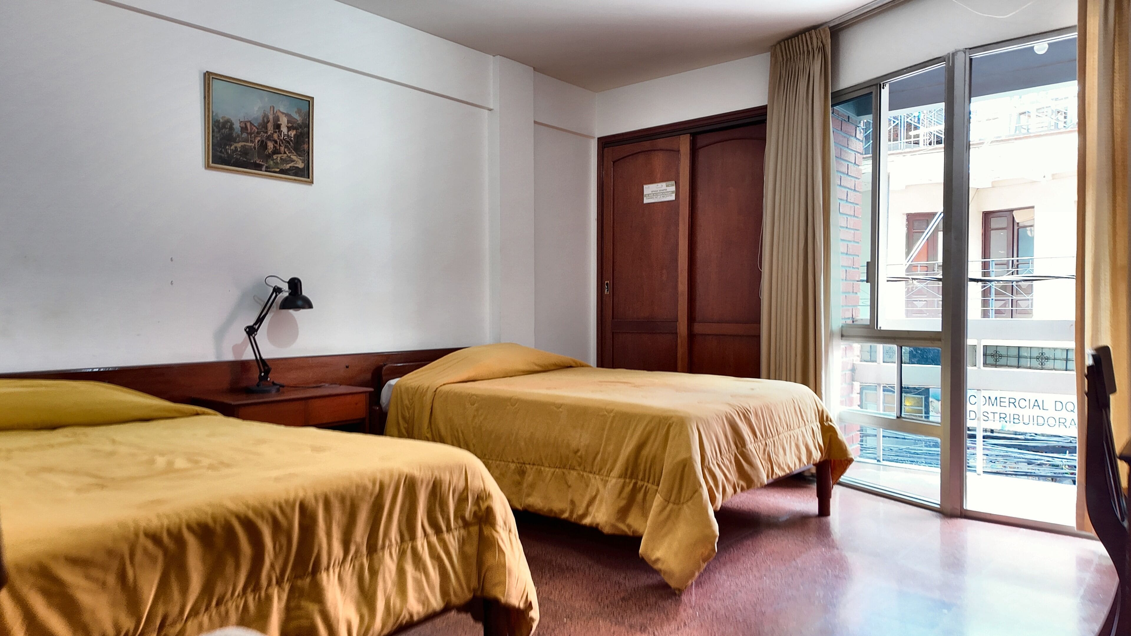 Une chambre d’hôtel avec deux lits, un bureau avec une lampe, une grande fenêtre et une porte.