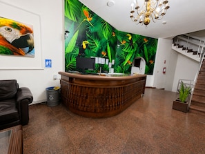 A reception desk with a monitor, a trash can, and a plant. - Gran Hotel Mediterráneo (Santa Cruz)