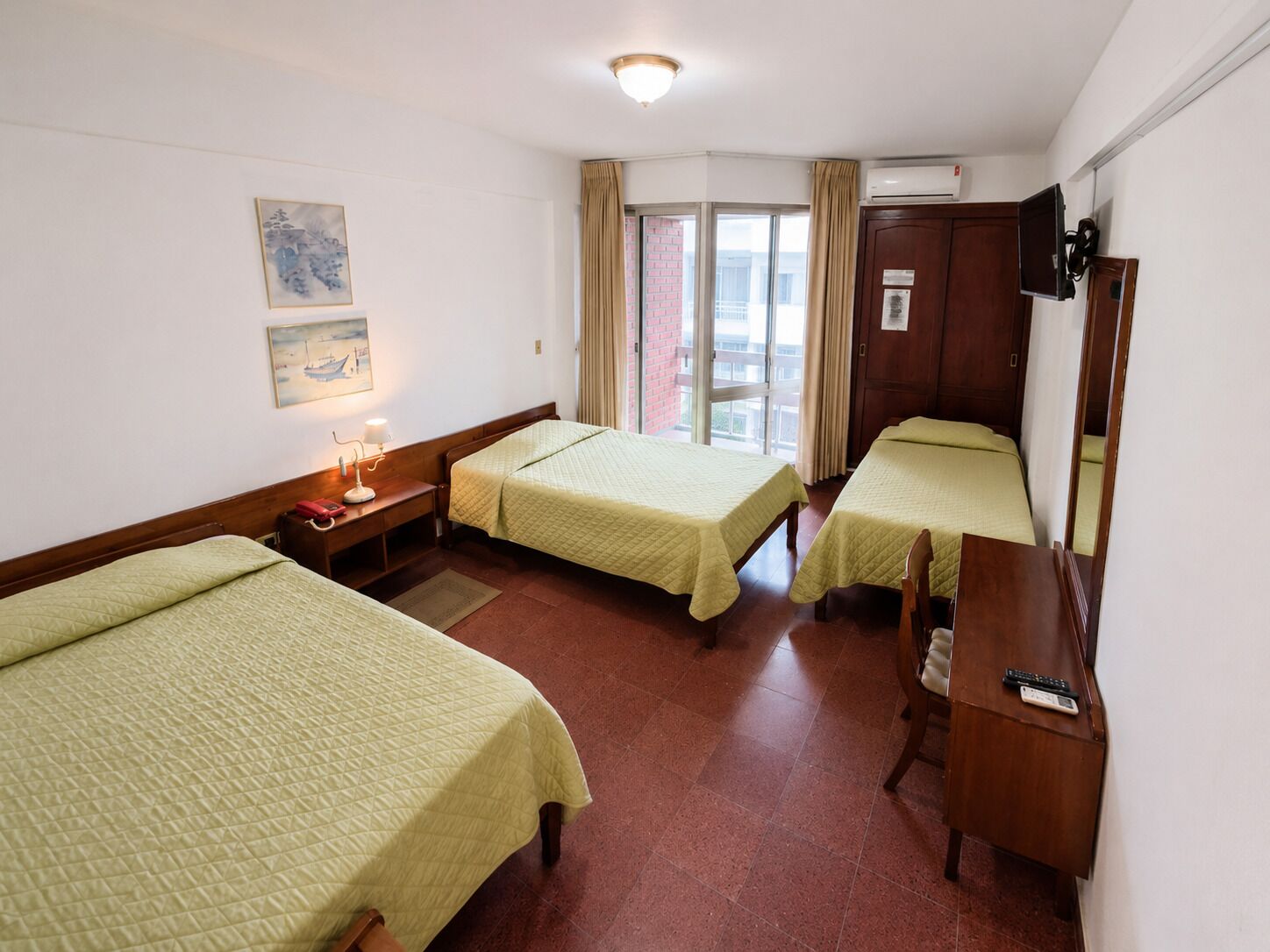Habitación de hotel con dos camas, un escritorio, una silla, un televisor y una ventana con cortinas.