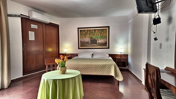 A hotel room with a bed, bedside tables, a desk with a chair, a table with a vase of flowers, and a painting on the wall. - Gran Hotel Mediterráneo (Santa Cruz)