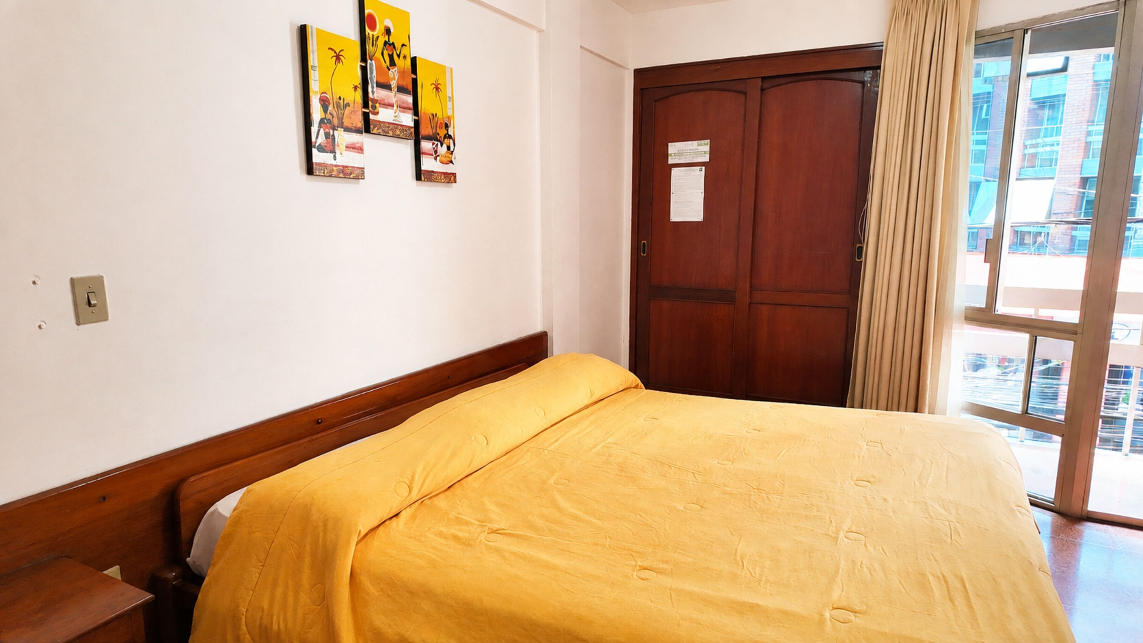 Habitación de hotel con cama, armario de madera, ventana con cortinas y decoración en la pared.
